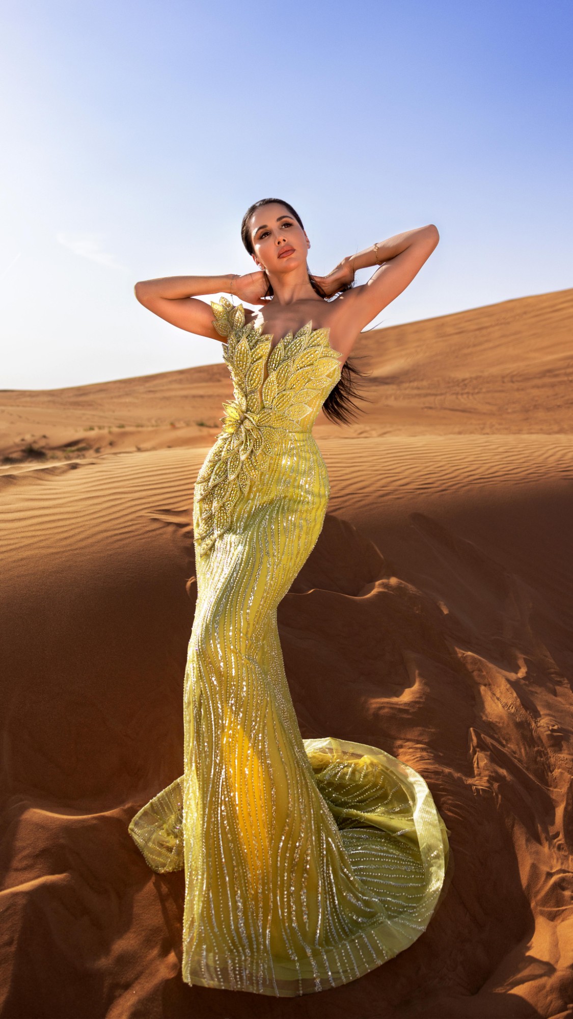 Somayeh dans les dunes, en robe sirène jaune brodée de feuilles, les bras levés derrière la tête