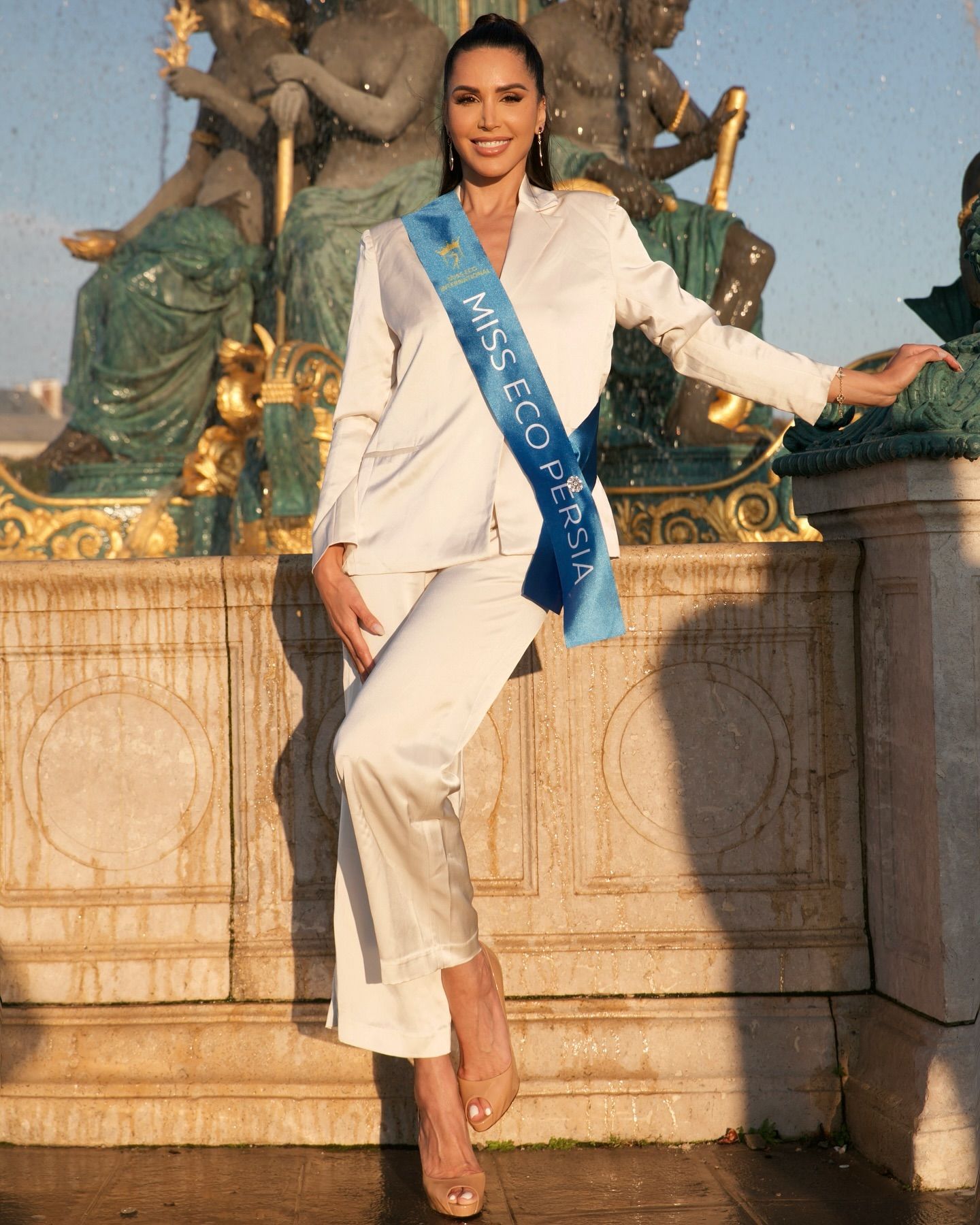 Somayeh devant une fontaine à Paris, en tailleur-pantalon ivoire, avec l’écharpe Miss Eco Persia
