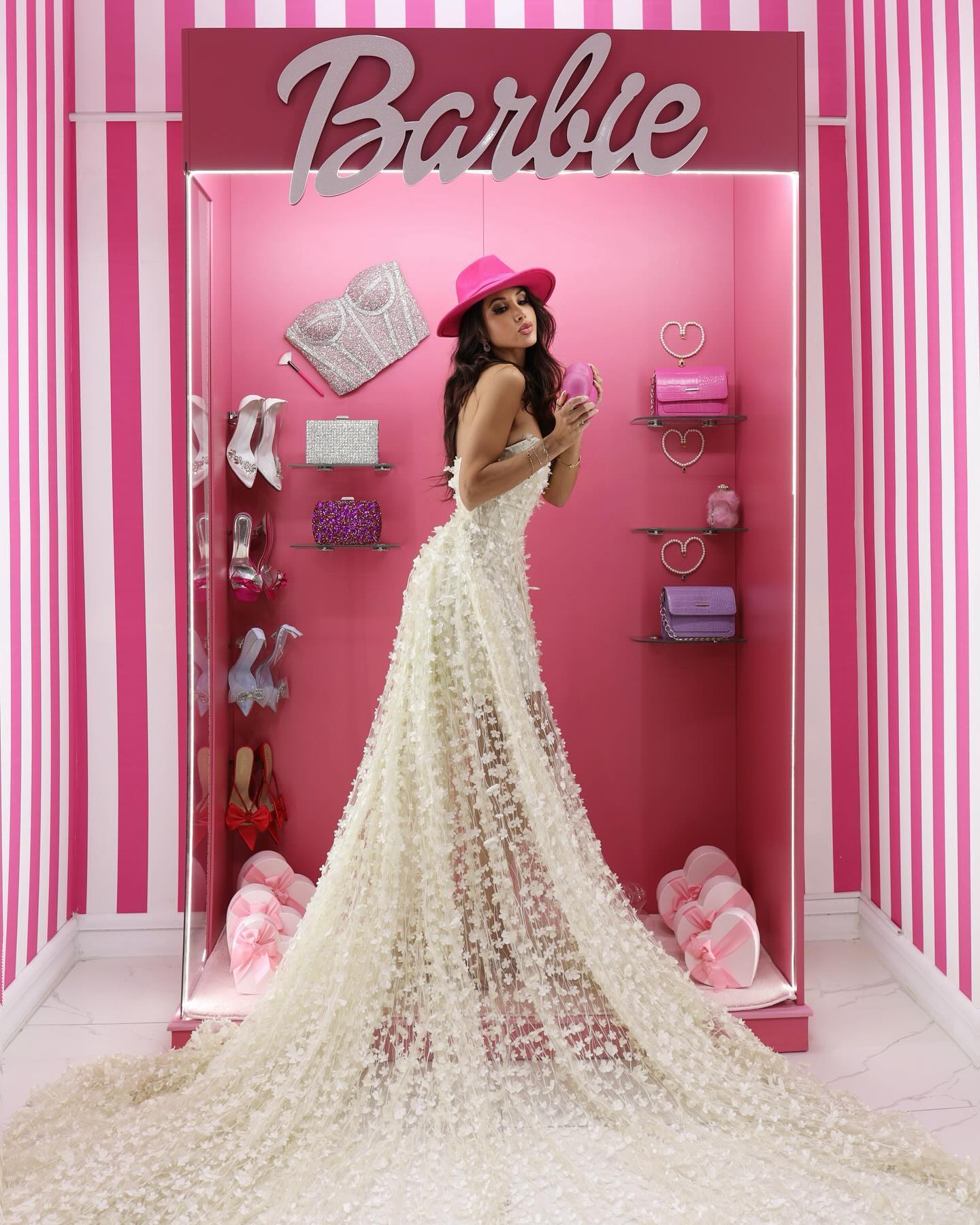 Somayeh dans un décor Barbie rose, en robe blanche à fleurs en relief et longue traîne, chapeau fuchsia