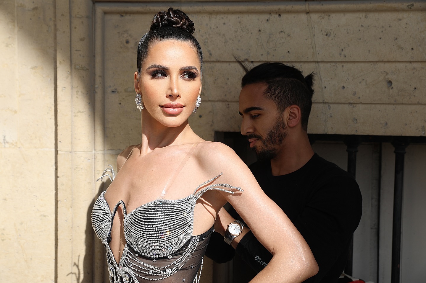 Somayeh en coulisses à Paris, en robe noire transparente ornée de cristaux, pendant qu’un styliste ajuste la tenue